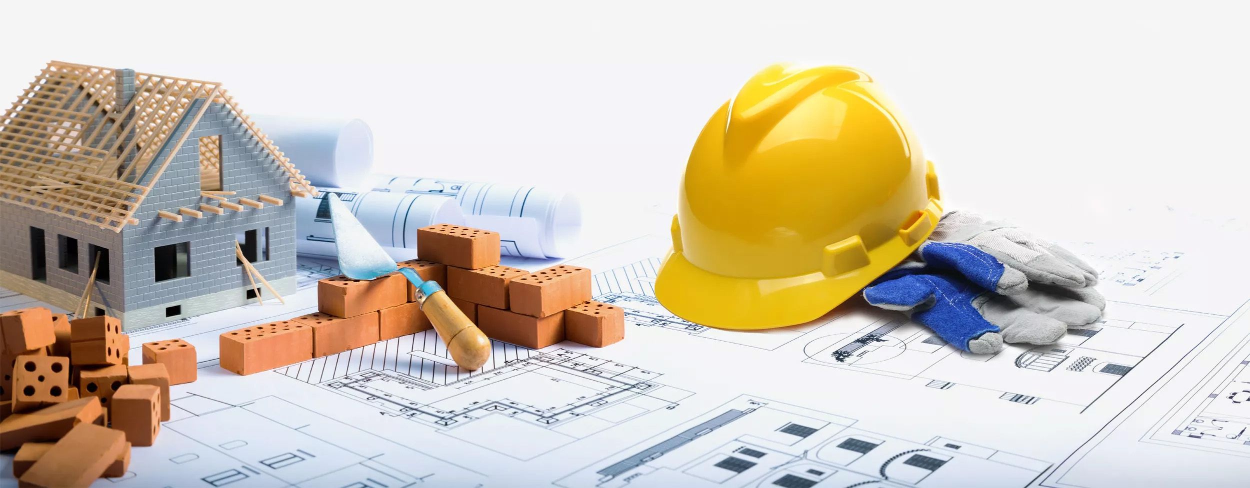 Ein großer Bauplan, wo ein Bauhelm draufliegt, ein Musterhaus draufsteht und andere Arbeitsmaterialien.